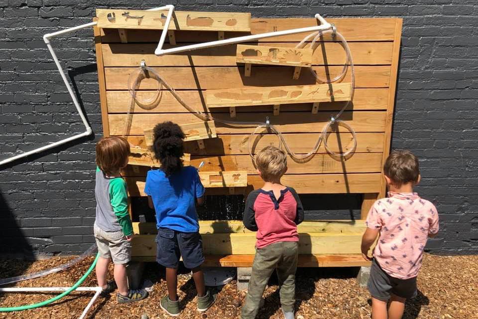 Children splash water at the water wall made of tubes, ramps, and a water fall.