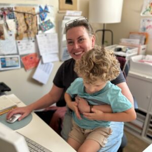 Angie holding a student while at her desk.
